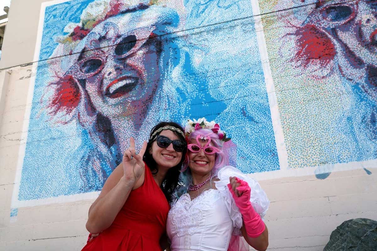 Image of Sugar Plump Fairy, Lemon Drop, standing in front of the mural she inspired.